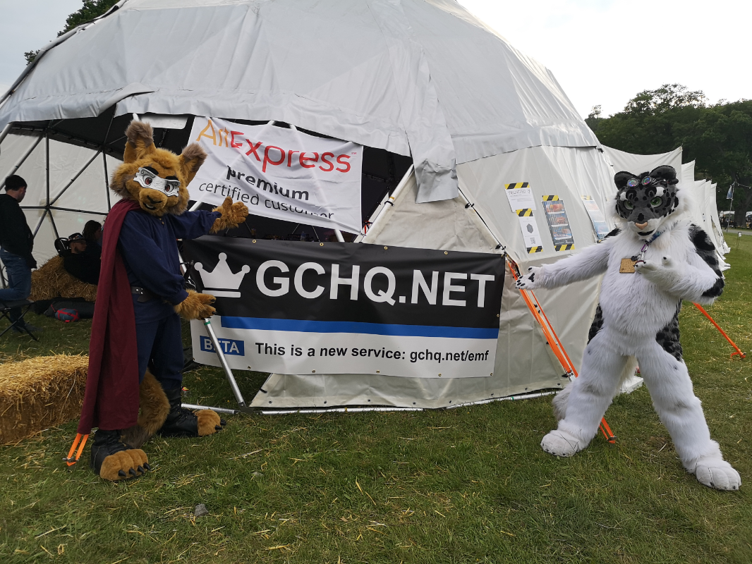 Cosmo and Gamepopper posing in suit in front of a sign that reads GCHQ dot net